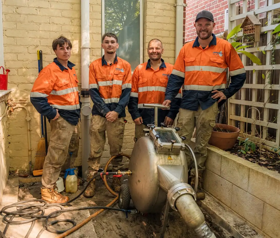 Four Pipe Relining Perth crew members standing beside their relining equipment at a heritage brick home.